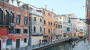 A canal-side walkway with historic buildings, a bridge, and a boat docked by the water. - Apartment Marin Venetian Style (Venecia)