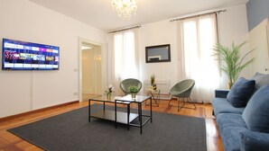 A living room with a flat-screen TV, a chandelier, a sofa, and two chairs.