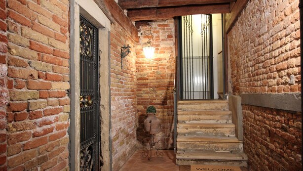A narrow brick corridor with a wooden staircase leading to a door marked "WELCOME".
