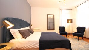 A neatly arranged bedroom with a large bed, two chairs, a small table, and a mirror on the wall.