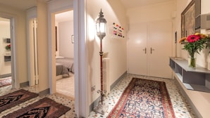 A hallway with a patterned rug, a radiator, a wall-mounted light fixture, and a shelf with flowers. - San Marco Central (100m from St Mark's Square) (Venecia)