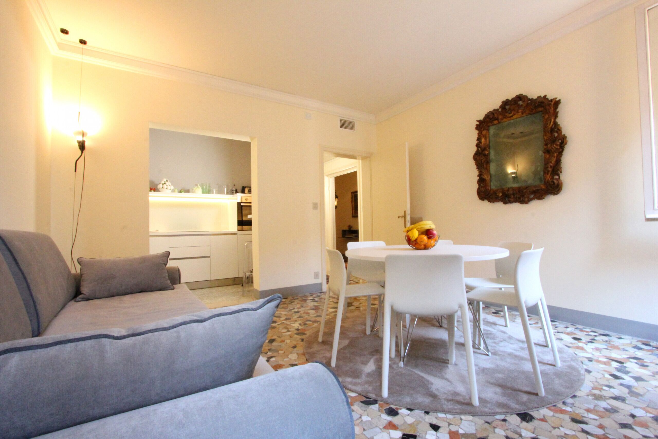 Un soggiorno moderno con un divano grigio, un tavolo da pranzo con sedie bianche e uno specchio decorativo appeso al muro.