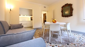 A modern living room with a grey sofa, a dining table with white chairs, and a decorative mirror on the wall. - San Marco Central (100m from St Mark's Square) (Venecia)