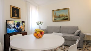 A living room with a round white table, a grey sofa, a TV on a wooden stand, and two paintings on the walls. - San Marco Central (100m from St Mark's Square) (Venecia)