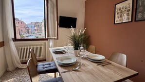 A dining table set with plates, glasses, and cutlery, a potted plant, and a view of a cityscape through a window. - Apt. Fosca Canal View (Venecia)