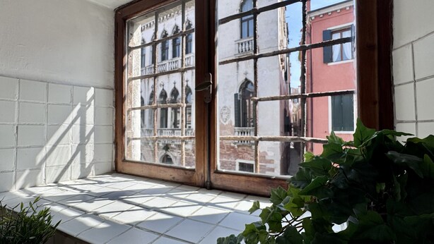 A window with a view of buildings, a tiled floor, and a plant in the foreground. - Apt. Fosca Canal View (Venecia)