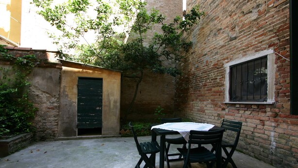 Une cour avec une table et des chaises, un mur de briques, une fenêtre et une porte.