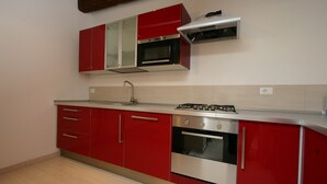 Une cuisine avec des armoires rouges, une hotte de cuisinière en acier inoxydable et un four encastré.