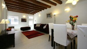 Un salon avec un tapis rouge, un canapé foncé, une table blanche avec des chaises et un vase de fleurs.