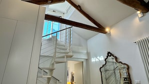 A staircase with a metal railing leading to a higher floor, a large mirror with an ornate frame, and a white radiator on the wall.