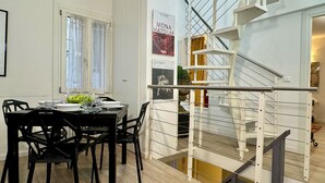A dining area with a table set for four, a staircase with a metal railing, and a poster on the wall.