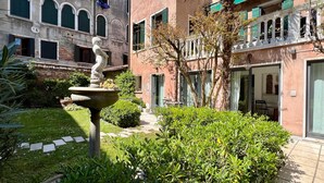 A courtyard with a fountain, lush greenery, and a building with arched windows and balconies. - Gelsomino Garden (Residence Flowery) (Venecia)