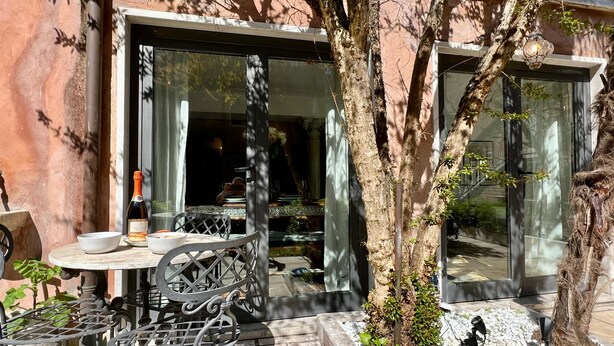 An outdoor dining area with a table and chairs, a bottle of wine, and a bowl of fruit. - Gelsomino Garden (Residence Flowery) (Venecia)