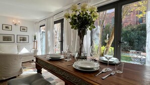 A dining area with a wooden table set for four, surrounded by white curtains and framed pictures on the walls. - Gelsomino Garden (Residence Flowery) (Venecia)