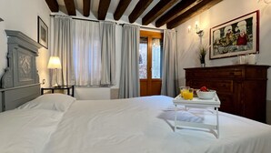 A hotel room with a bed, a nightstand with a lamp, a dresser, a painting, and a breakfast tray with orange juice and a bowl. - Gelsomino Garden (Residence Flowery) (Venecia)