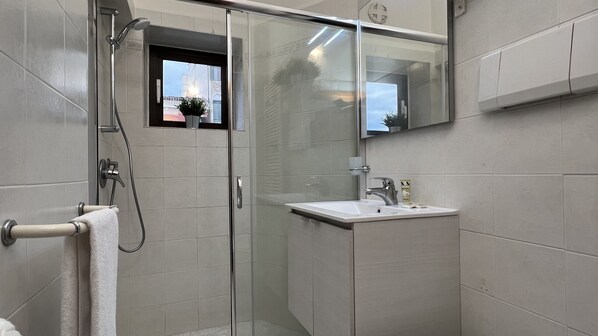A modern bathroom with a glass shower enclosure, a white sink, and a large mirror.
