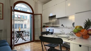 Una cocina moderna con armarios blancos, un comedor con mesa dispuesta para dos personas y un balcón con mesa y sillas.