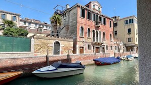 A canal with boats docked, a stone wall, and buildings with arched windows and balconies.