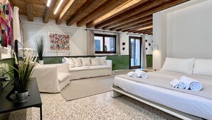 A hotel room with a bed, a sofa, a small table with a plant, and a painting on the wall.