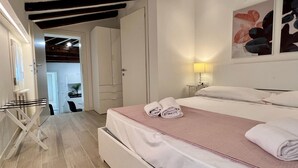 A hotel room with a bed, a bedside table with a lamp, a wardrobe, and a view of a dining area. - Relax Terrace (Venice Historical Center) (Venecia)