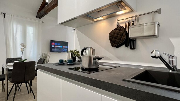 A modern kitchen with a black countertop, stainless steel kettle, and a flat-screen TV mounted on the wall. - Relax Terrace (Venice Historical Center) (Venecia)
