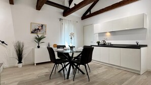 A modern kitchen with white cabinets, a black countertop, and a dining area with a glass table and black chairs. - Relax Terrace (Venice Historical Center) (Venecia)