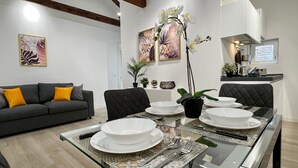 A modern dining area with a glass table set for four, surrounded by dark upholstered chairs. A grey sofa with yellow cushions is in the foreground, and a kitchen area is visible to the right. - Relax Terrace (Venice Historical Center) (Venecia)