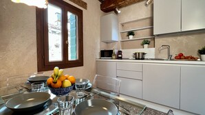Une cuisine moderne avec des meubles blancs, une table à manger dressée avec des assiettes, des bols et des verres, et une fenêtre donnant sur les bâtiments environnants.