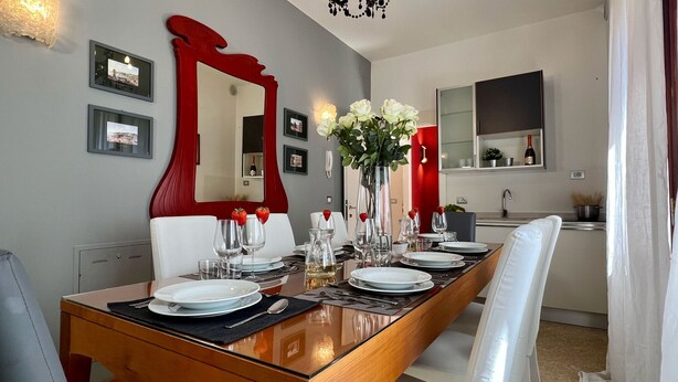 A dining area with a wooden table set for four, surrounded by white chairs. A large mirror and framed pictures adorn the walls.