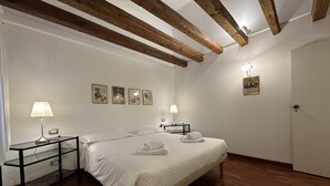 A hotel room with a wooden ceiling, a bed with white linens, two bedside tables with lamps, and framed pictures on the wall.