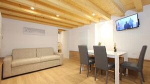 A room with a wooden ceiling, a beige sofa, a dining table with chairs, and a television mounted on the wall. - Apt. Ca'Puccetti Bis (350mt from Rialto's Bridge) (Venecia)