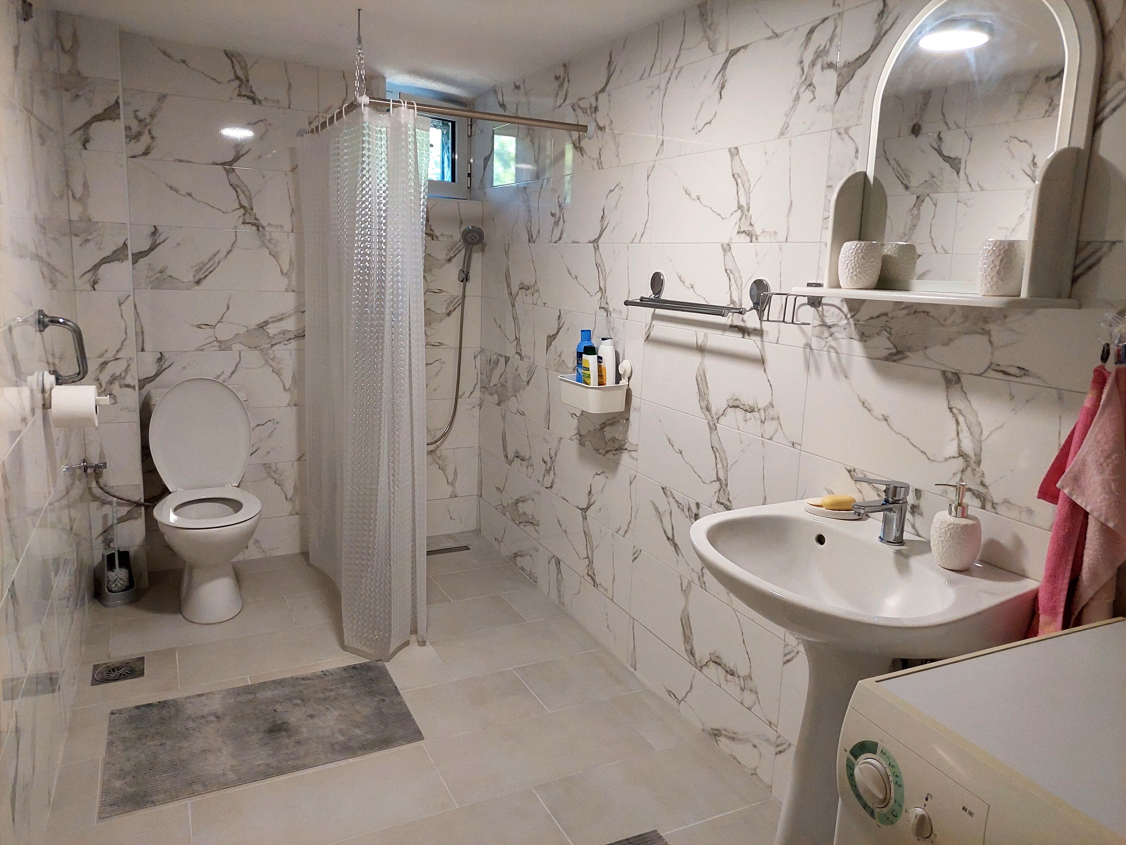 Un baño con inodoro, ducha, lavabo y paredes de mármol.