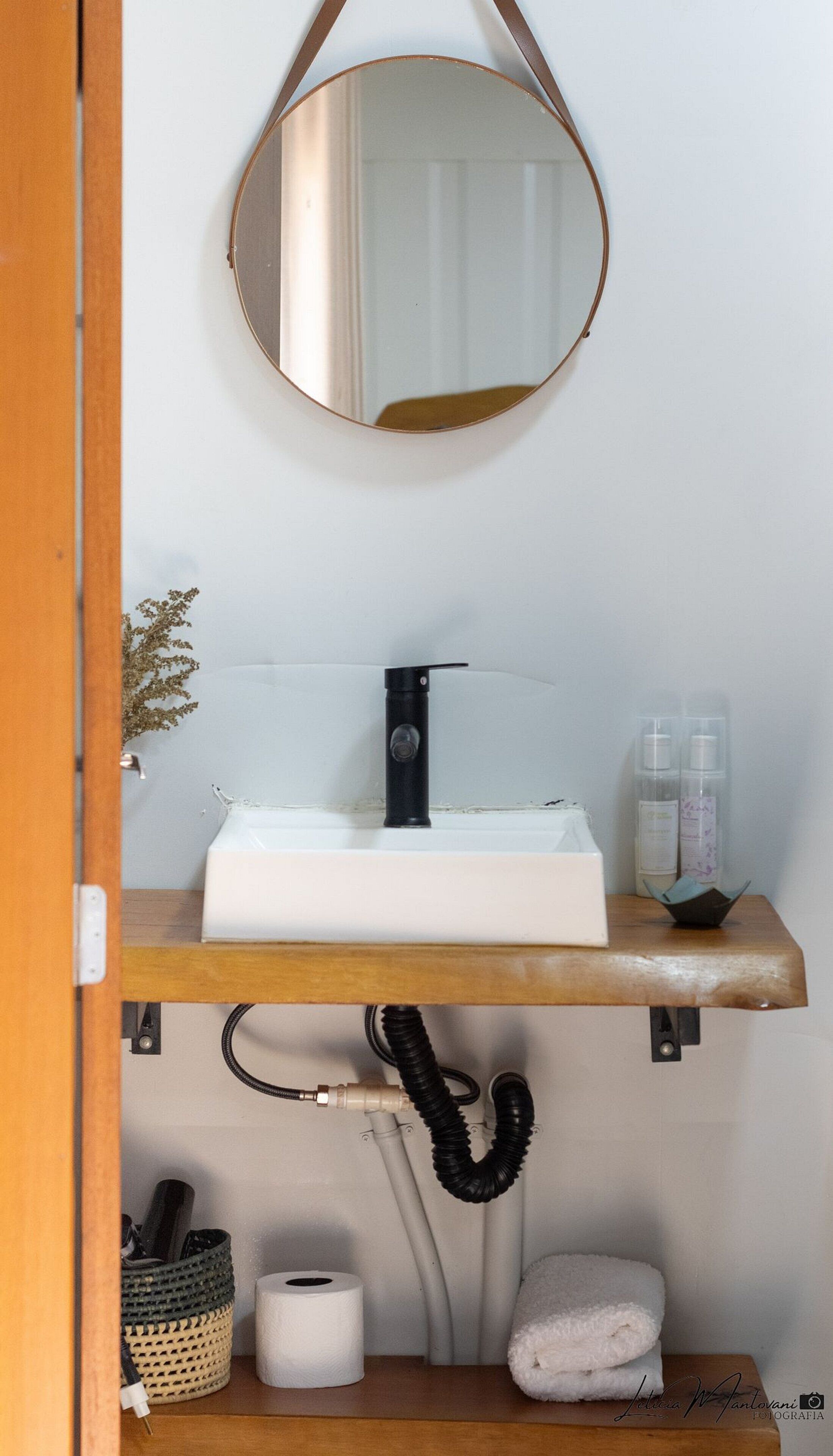 Un baño con tocador de madera, un lavabo blanco, un grifo negro, un espejo y una toalla.