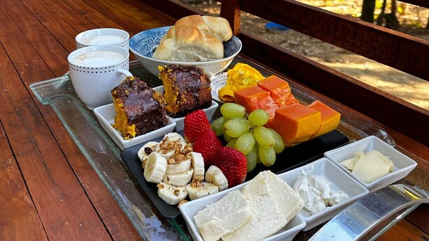 A picnic setup with food items on a tray, including bread, fruits, and desserts, on a wooden deck with a railing. - Recanto das Videiras - container (Itapira)