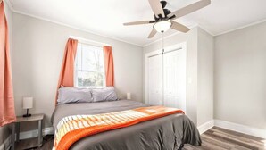 Een slaapkamer met een bed, een plafondventilator, een nachtkastje, een raam met gordijnen en een deur.