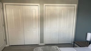 Une chambre à coucher avec un lit, deux portes blanches, une table de chevet et une lampe.