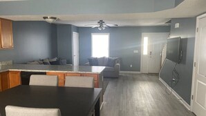 Une cuisine moderne avec un coin repas, un canapé gris et un ventilateur de plafond.