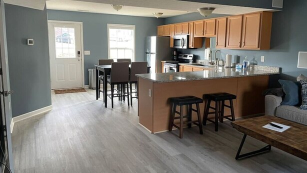 A modern kitchen with a central island, wooden cabinets, and a dining area with chairs. - Luxury Townhome #2  - Remodeled Feb 2021 (Bloomington)