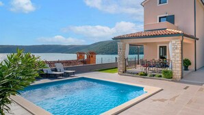 Una villa moderna con piscina, mobiliario exterior y vistas al lago.