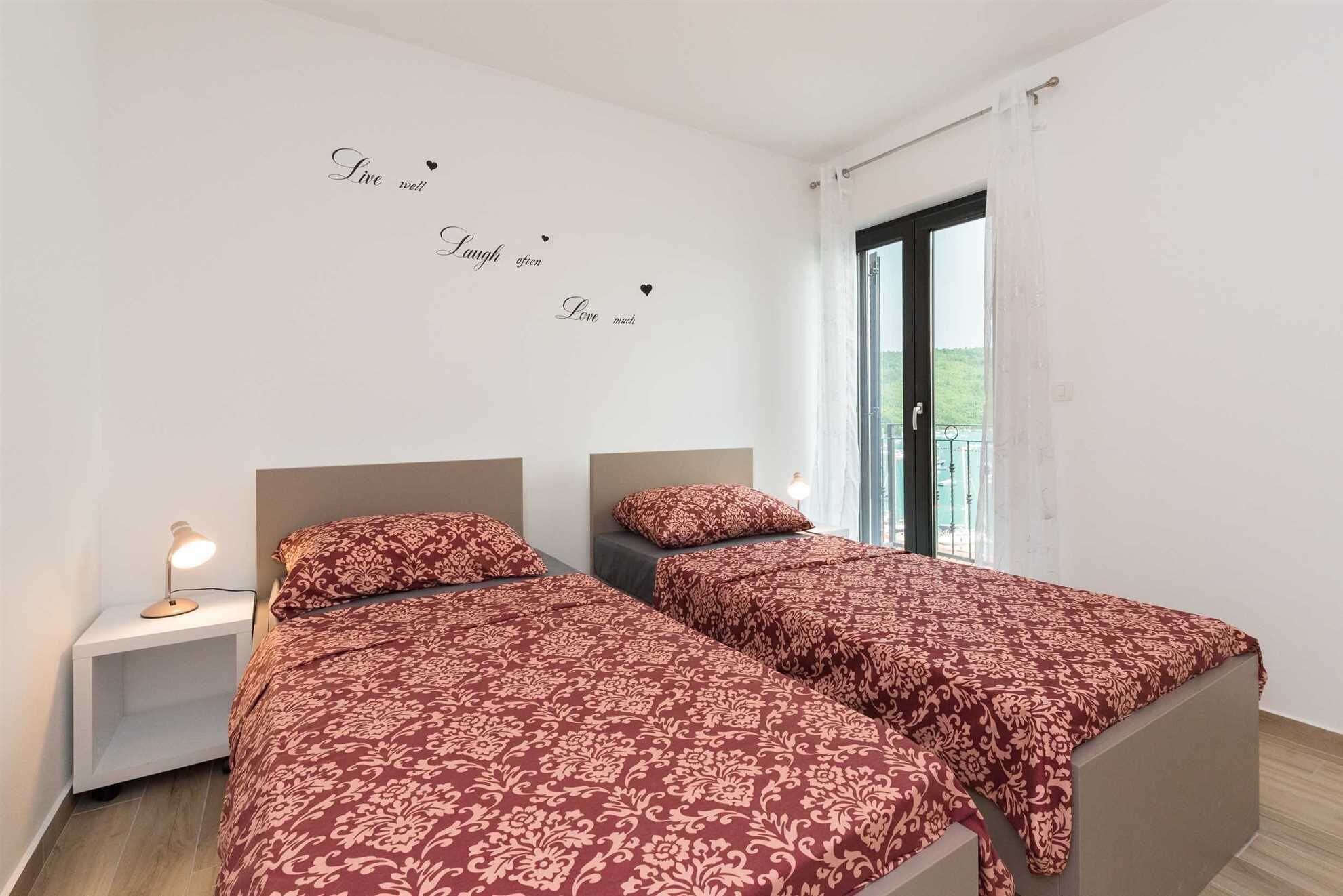 Un dormitorio con dos camas, una mesita de noche con lámpara y una ventana con vista a zonas verdes.