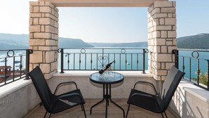 Un balcón con dos sillas y una mesa, con vista a un lago con barcos y colinas al fondo.