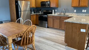 A kitchen with wooden cabinets, stainless steel appliances, a granite countertop, and a dining area with wooden chairs.