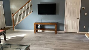 A living room with a wooden bench, a TV mounted on the wall, and a staircase.
