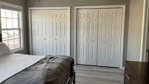 A bedroom with a bed, two white doors, a dresser, and a window with blinds.