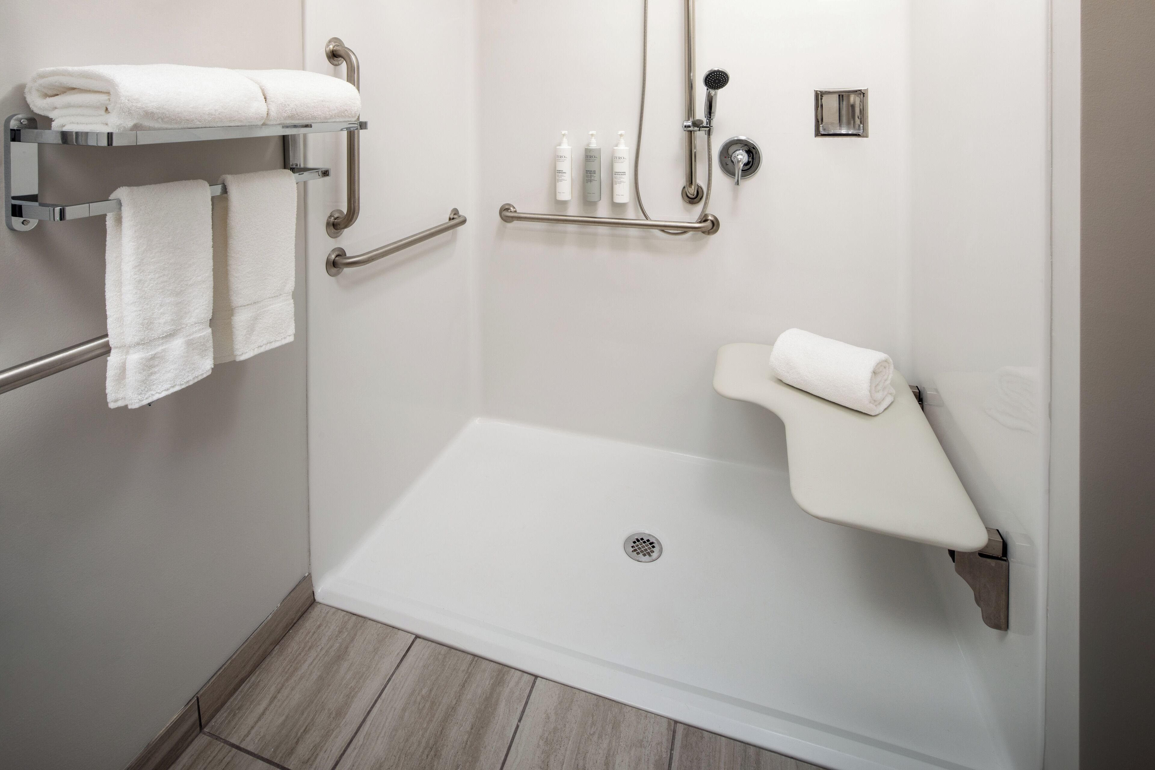 A modern bathroom with a walk-in shower, grab bars, and a towel rack.