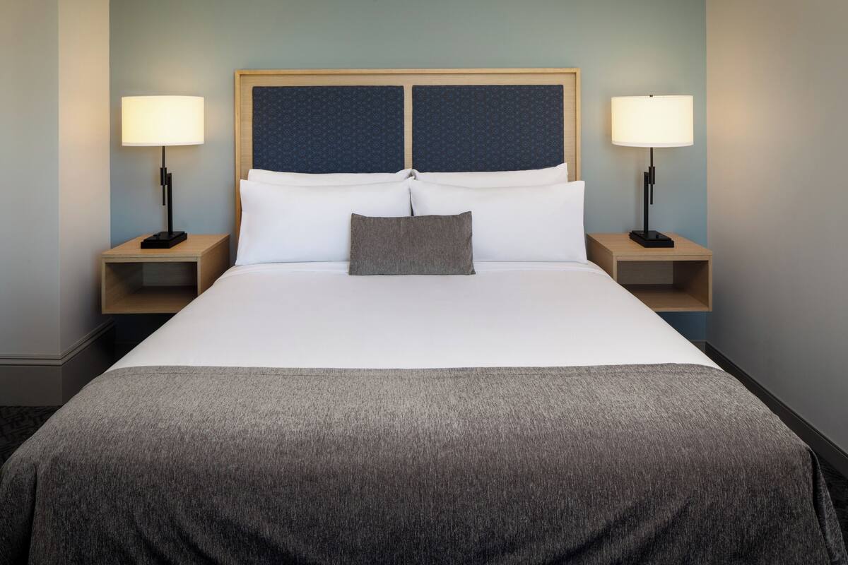 A neatly made bed with a grey blanket, two bedside lamps, and a headboard with a blue panel.