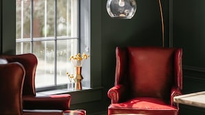 A room with a large window, a red leather armchair, a small table with a vase of yellow flowers, and a hanging spherical light fixture. - Hotel Ursa (Orono)
