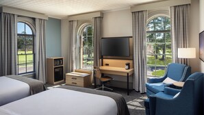 A hotel room with two beds, a desk, a chair, a TV, and large windows with curtains. - Hotel Ursa (Orono)