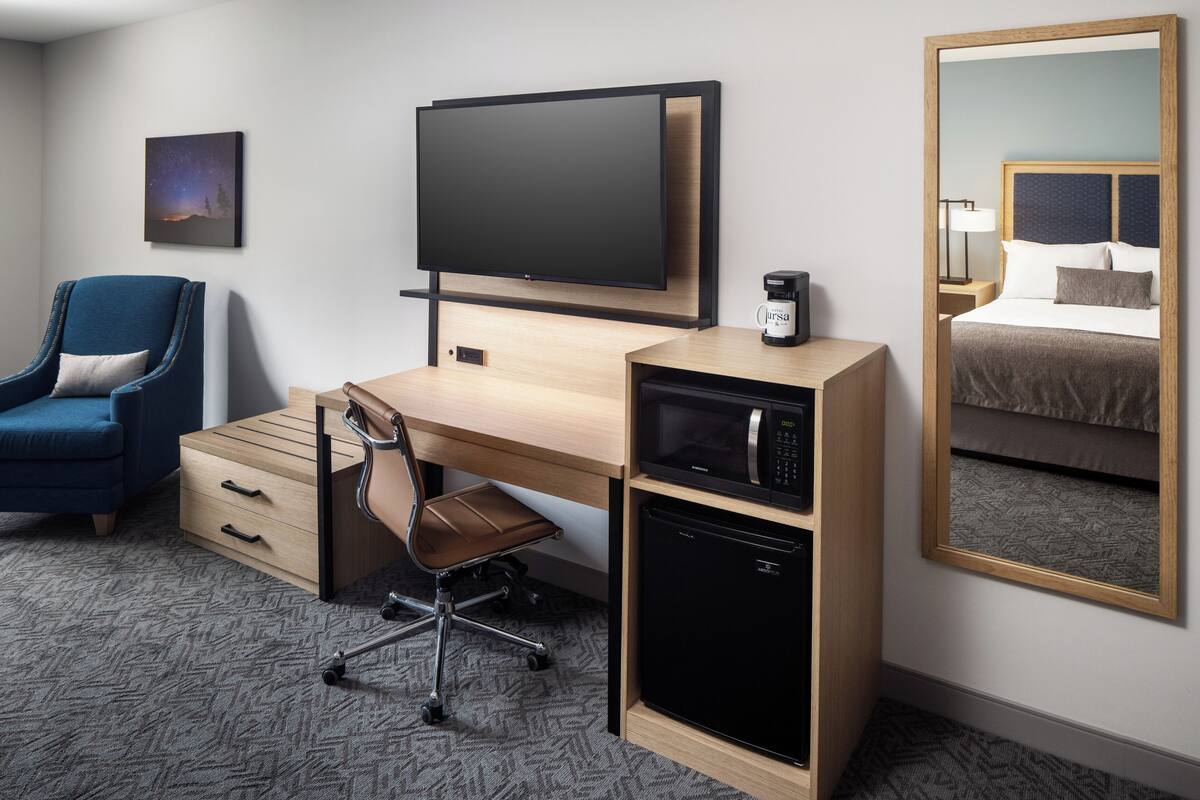 A hotel room with a wooden desk, a television, a coffee maker, a microwave, and a bed with a headboard.