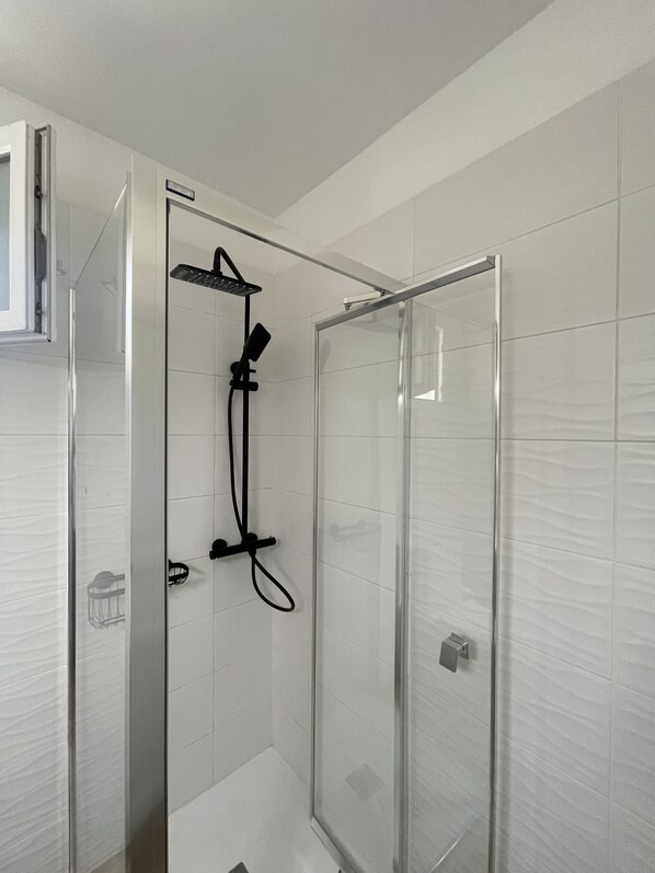 Ein modernes Badezimmer mit einer Duschkabine aus Glas, weißen Fliesenwänden und einem sichtbaren Türgriff.